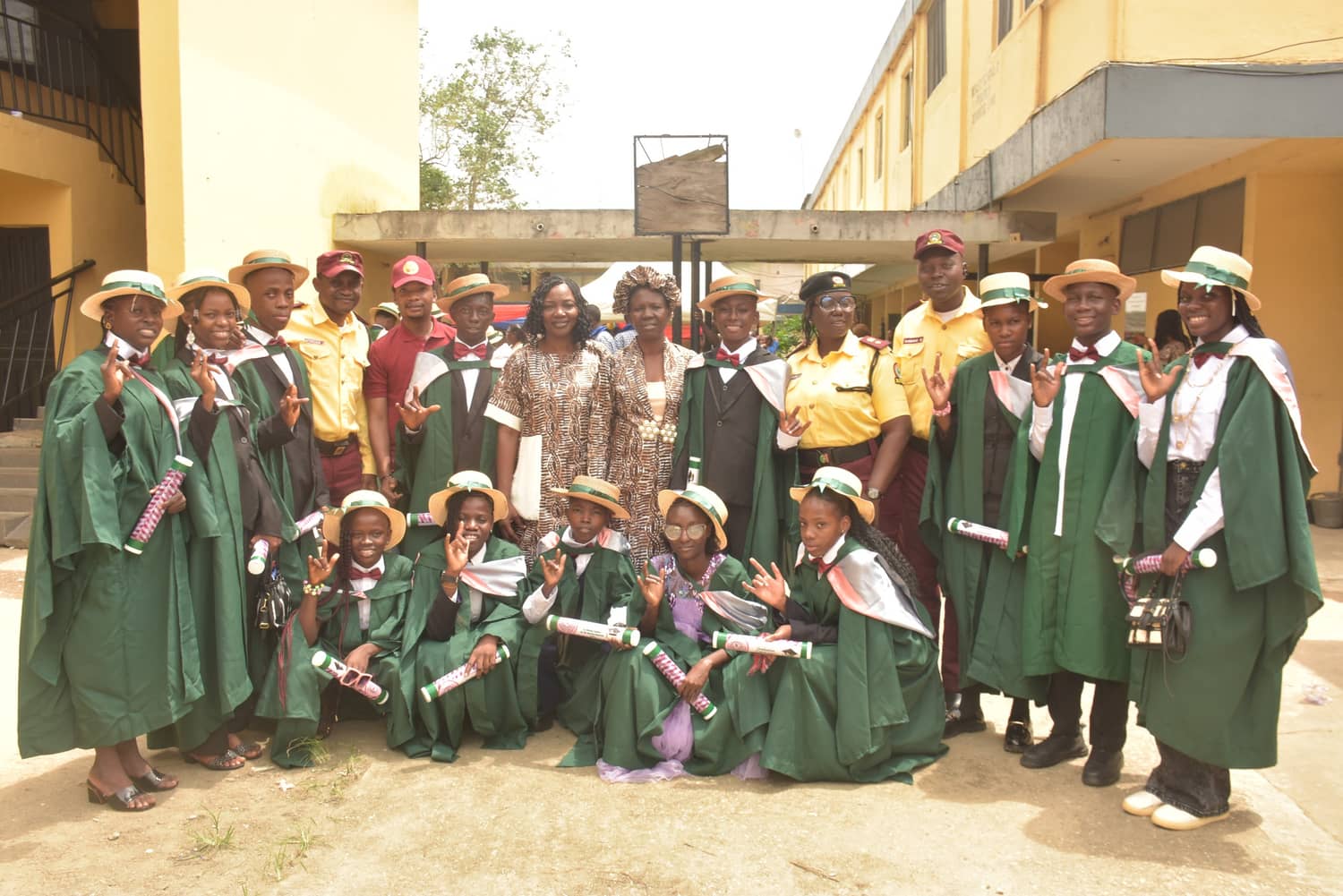 Graduating pupils of a school for the hearing impaired in green gowns sign 'I love you' alongside LASTMA officers and their teachers