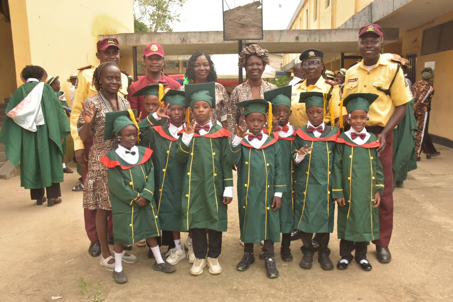The youngest graduates in green gowns and mortarboards, some signing to the camera, with LASTMA officers behind them